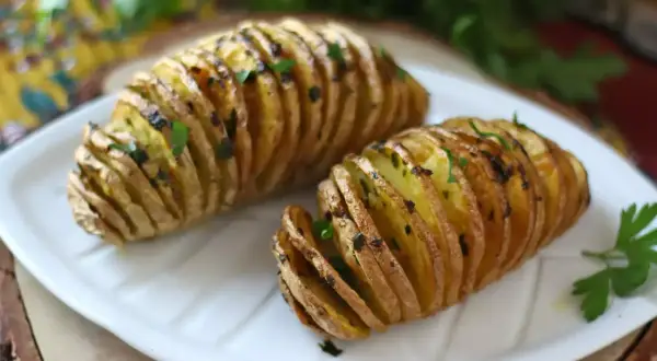 Två gyllene hasselbackspotatis med parmesan och färska örter på en vit tallrik.