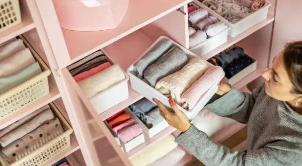 Donna sistema maglioni e calzini in contenitori per organizzare spazi casa. Armadio rosa ordinato con vestiti piegati.