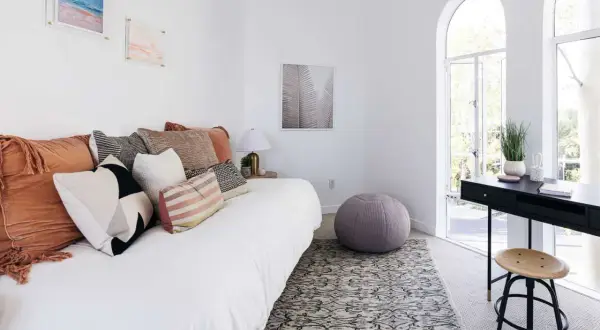 A white daybed piled with plush pillows sits in a bright room with arched windows.
