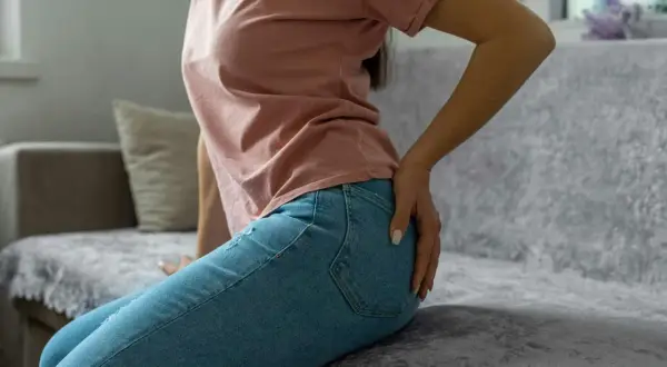 Person sitter på en soffa och håller sig om höften, med en tydlig känsla av ont under rumpan.