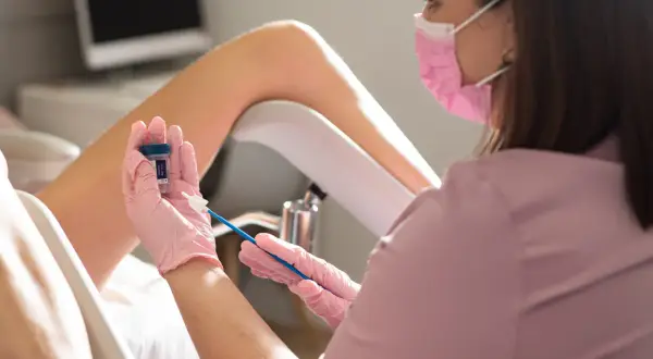 Lekarka w różowej masce i rękawiczkach przygotowuje się do pobrania wymazu. Czy cytologia boli? To badanie jest zazwyczaj bezbolesne.