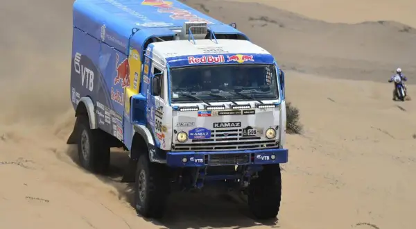 Camion Kamaz aux couleurs Red Bull, prêt à affronter le désert. La puissance camion Dakar se révèle dans ce paysage sablonneux.