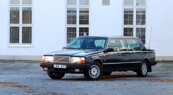 Svart, förlängd 760 Volvo med blåljus på taket, parkerad framför en vit byggnad med stora fönster.