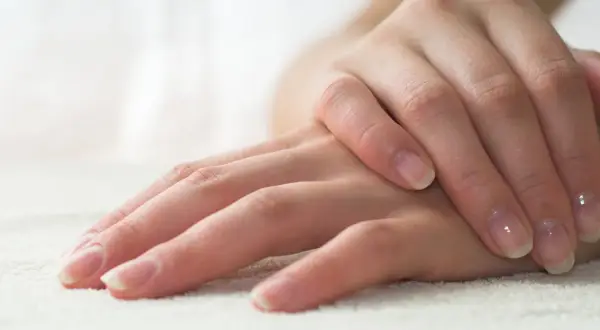 Delikatne dłonie z naturalnym, błyszczącym manicurem biologicznym. Paznokcie zadbane, z subtelnym połyskiem.