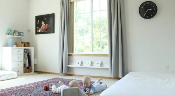 Two babies explore a room with a Montessori inspired feel, featuring a rug, toy basket, and artwork.