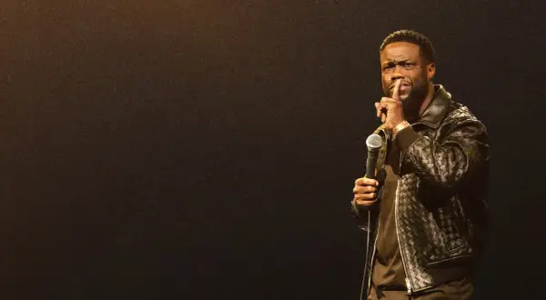 Kevin Hart stand up, trzymając mikrofon i gestykulując do publiczności.
