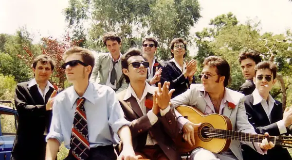 Grupo de hombres con trajes, uno toca la guitarra, listos para una rumba catalana bajo el sol.