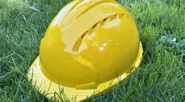Żółty kask ochronny leży na trawie. Pamiętaj o sprawdzeniu **daty ważności kasku ochronnego** przed użyciem.