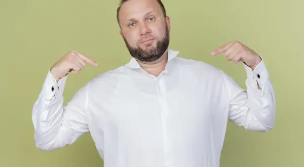 Mann zeigt auf sich und sein weißes Hemd. Er fragt sich, welches Unterhemd unter dem Hemd am besten passt.
