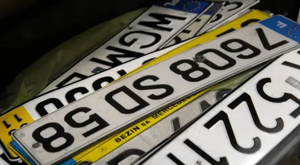 Stos tablic rejestracyjnych, w tym jedna z napisem "BEZIN SA MERCEDES". Widać fragmenty numerów, np. 8509L, 85DS, WGM.