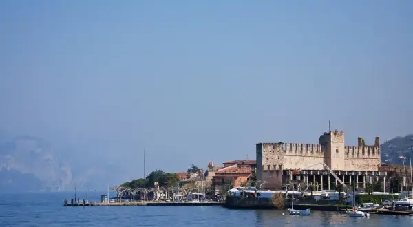 Rocchetta di Moniga del Garda, un gioiello da vedere sul lago. Passeggiata sul lungolago con barche e montagne sullo sfondo.