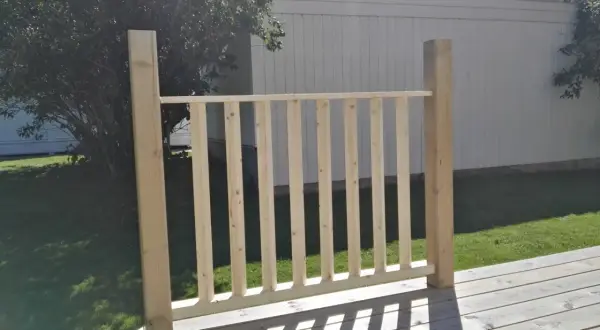 Nybyggt räcke med plank stående ribbor på en altan. Solen kastar skuggor över träet.
