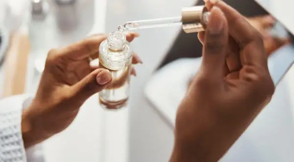 Dłonie trzymają buteleczkę z serum. Pipeta z kroplą produktu, być może zawierającego kwas ferulowy, jest gotowa do aplikacji.