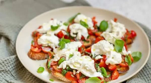 Bruschetta med burrata, färska tomater och basilika på en tallrik.