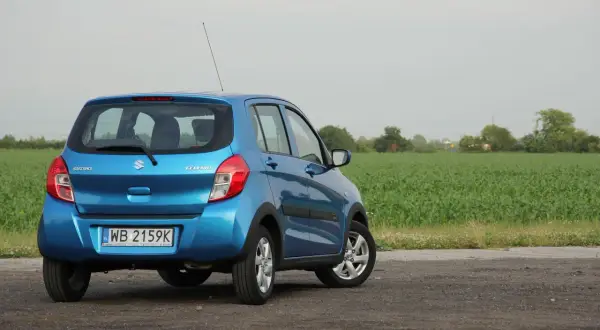 Niebieski Suzuki Celerio zaparkowany na drodze polnej, z polem kukurydzy w tle.