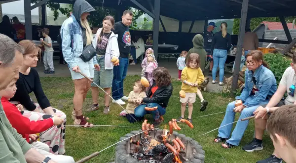 Rodzina piecze kiełbaski nad ogniskiem, czuć puls miasta w tej sielskiej atmosferze.