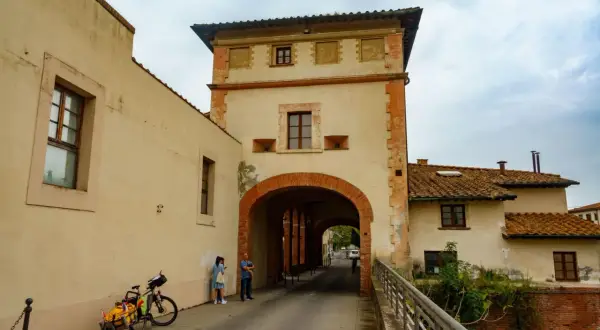 Pieve a Nievole: un arco in mattoni rossi conduce a una strada con case antiche. Una coppia e una bici con carretto attendono.