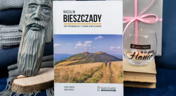 Książki o Bieszczadach zachęcają do podróży. Na okładce przewodnik po Bieszczadach, obok rzeźba i świeca.