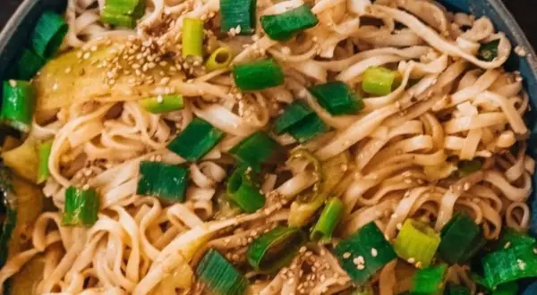 Schüssel mit Udon-Nudeln, garniert mit Frühlingszwiebeln und Sesam. Ein einfaches Udon-Nudel-Rezept, das schnell zubereitet ist.