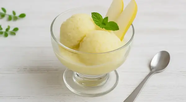 Ein Glas mit cremigem Birnen-Eis, garniert mit frischer Minze und Birnenspalten. Perfekt für einen heißen Sommertag.
