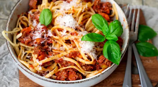 Eine Schüssel mit Linguine und einer herzhaften, **schnellen Bolognese**, garniert mit frischem Basilikum und Parmesan.
