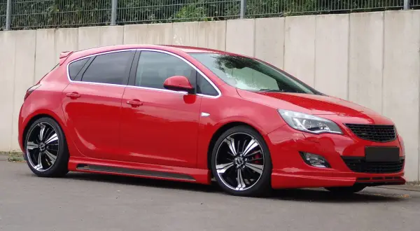 Czerwony Opel Astra J z przyciemnianymi szybami i efektownymi felgami. Widać jego światła pozycyjne.