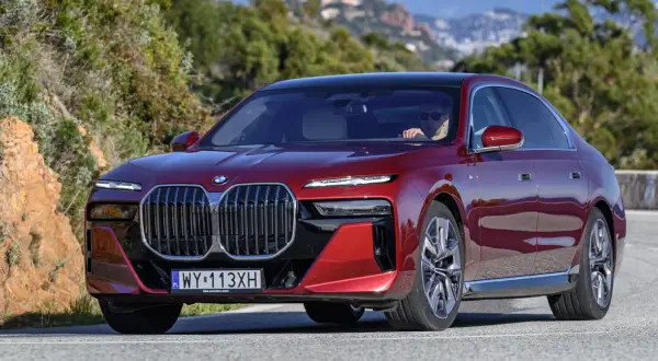 Czerwone BMW serii 7 z kierowcą za kierownicą, jadące po krętej drodze.