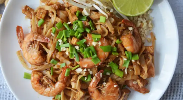 Pyszny pad thai kung z krewetkami, tofu i szczypiorkiem, podany z kiełkami fasoli mung i ćwiartką limonki.