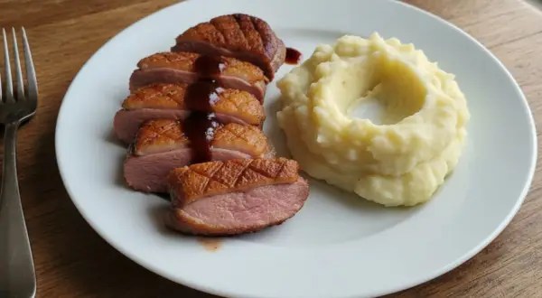 Soczysta pierś z kaczki, pokrojona w plastry, polana sosem, obok porcja purée ziemniaczanego.