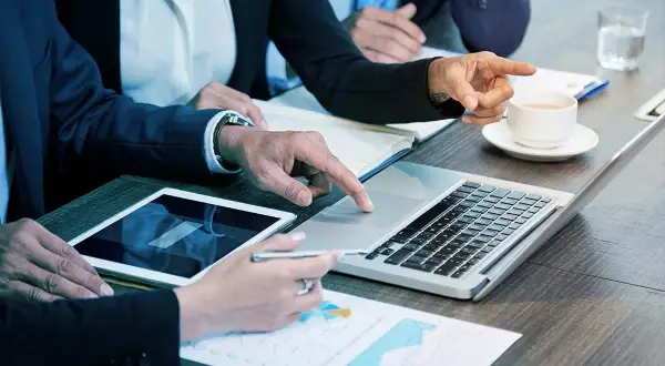 Persone in abiti eleganti collaborano a un tavolo, analizzando dati su tablet e laptop. Sono le risorse umane che lavorano insieme per il successo.