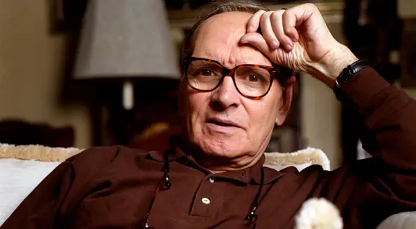 Ennio Morricone, genius kompozytor muzyki do **ennio morricone filmy**, zamyślony z ręką na czole.