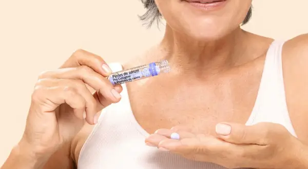 Une femme tient une perle de sérum contenant des peptides, prête à l'appliquer pour un soin anti-âge.