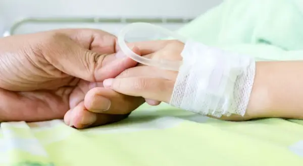 Dłoń rodzica trzyma dłoń dziecka w szpitalu, gdzie wystawiane jest zwolnienie na dziecko w szpitalu.