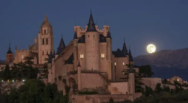 El majestuoso castillo de Segovia se alza bajo una luna llena, con su imponente arquitectura y torres que parecen vigilar la noche.