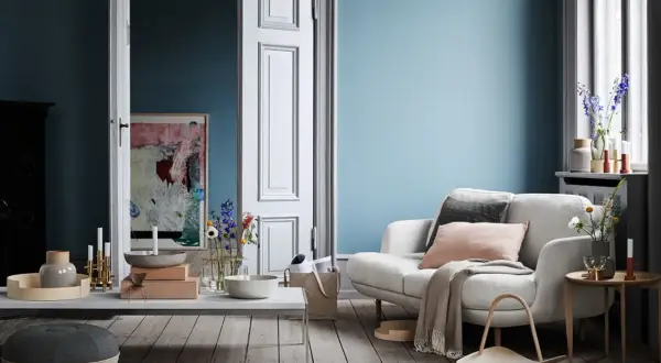 Ein gemütliches Wohnzimmer mit einer hellblauen Wand, einem weißen Sofa, Kissen, Decke und einem Beistelltisch.