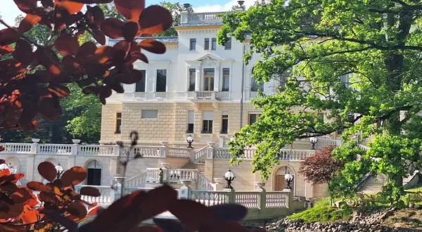 Pałac Heinzel w Łagiewnikach otoczony zielenią, z widokiem na staw i ozdobne schody.