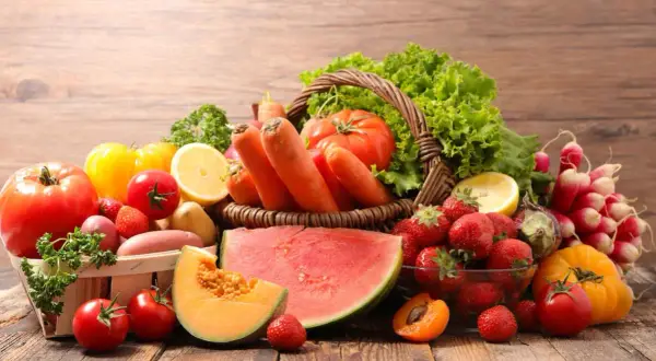 Un cesto traboccante di frutta di stagione giugno: fragole, melone, albicocche, anguria, carote, pomodori, lattuga e limone.