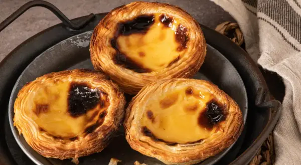 Trzy pyszne portugalskie ciastka, znane jako pastéis de nata, z chrupiącym ciastem i kremowym, lekko przypieczonym nadzieniem.
