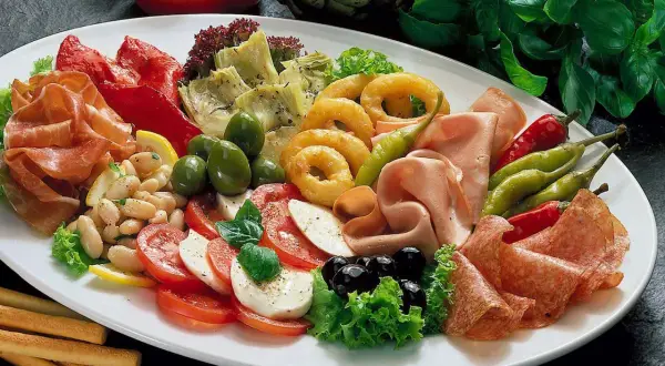 Eine reichhaltige Antipasti-Platte mit Wurst, Käse, Gemüse, Oliven und Brotstangen.