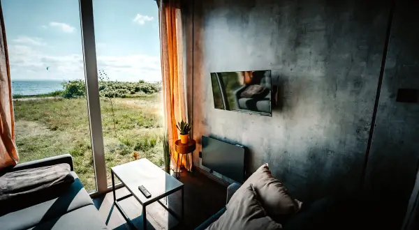 Nowoczesny salon z widokiem na zatokę pucką. Kanapa, stolik i telewizor na tle betonowej ściany.