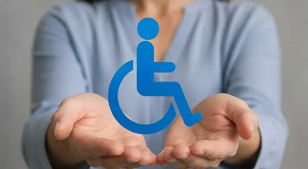 Hände halten ein blaues Rollstuhlsymbol. Nützliche Tipps für den Antrag auf Schwerbehinderung.