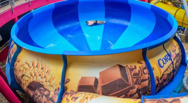 Mann rutscht in einer riesigen blauen Schüssel einer Wasserrutsche, die mit Schokolade und Getreide dekoriert ist. Ein Spaß im Prag!