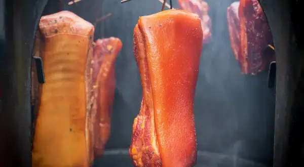Fleischstücke hängen im Rauch, bereit für das **bacon selber machen**. Der Prozess des Räucherns verleiht dem Speck seine charakteristische Farbe und Aroma.