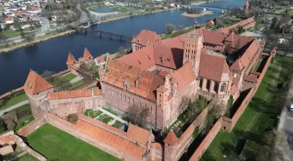 Malbork, największy zamek na świecie, rozciąga się wzdłuż rzeki Nogat. Potężne ceglane mury i wieże świadczą o jego historycznym znaczeniu.