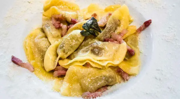 Deliziosi ravioli bresciani conditi con pancetta croccante e una foglia di salvia, spolverati di parmigiano.