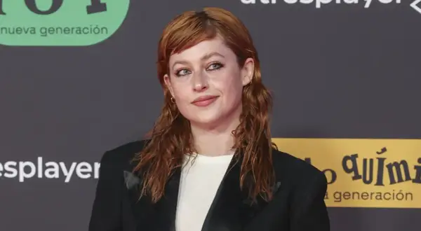 Chloe Wallace, con su cabello pelirrojo y mirada cautivadora, posa con un blazer negro.