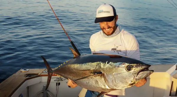 Glücklicher Angler hält stolz einen riesigen Thunfisch, den er beim Thunfisch angeln gefangen hat. Das Boot schaukelt sanft auf dem Meer.