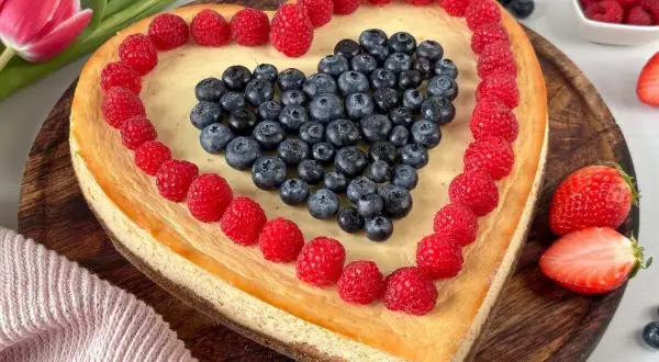 Herzförmiger Kuchen zum Muttertag, dekoriert mit Himbeeren und Blaubeeren. Ein süßes Dankeschön für Mama.