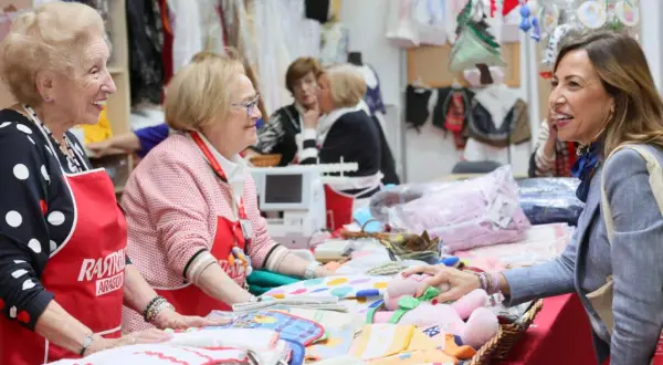 Sonríen vendedoras en el mercadillo Ozanam Zaragoza, mostrando textiles y peluches.
