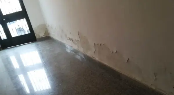 Pared con pintura descascarada y manchas de humedad por capilaridad cerca de la puerta. Es necesario reparar la pared.